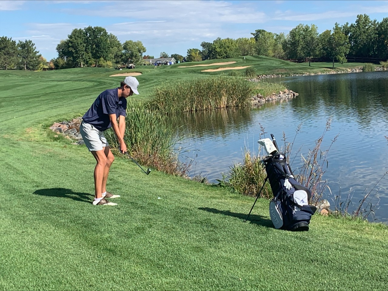 An AAHS Golf player lines up a shot near a pond.